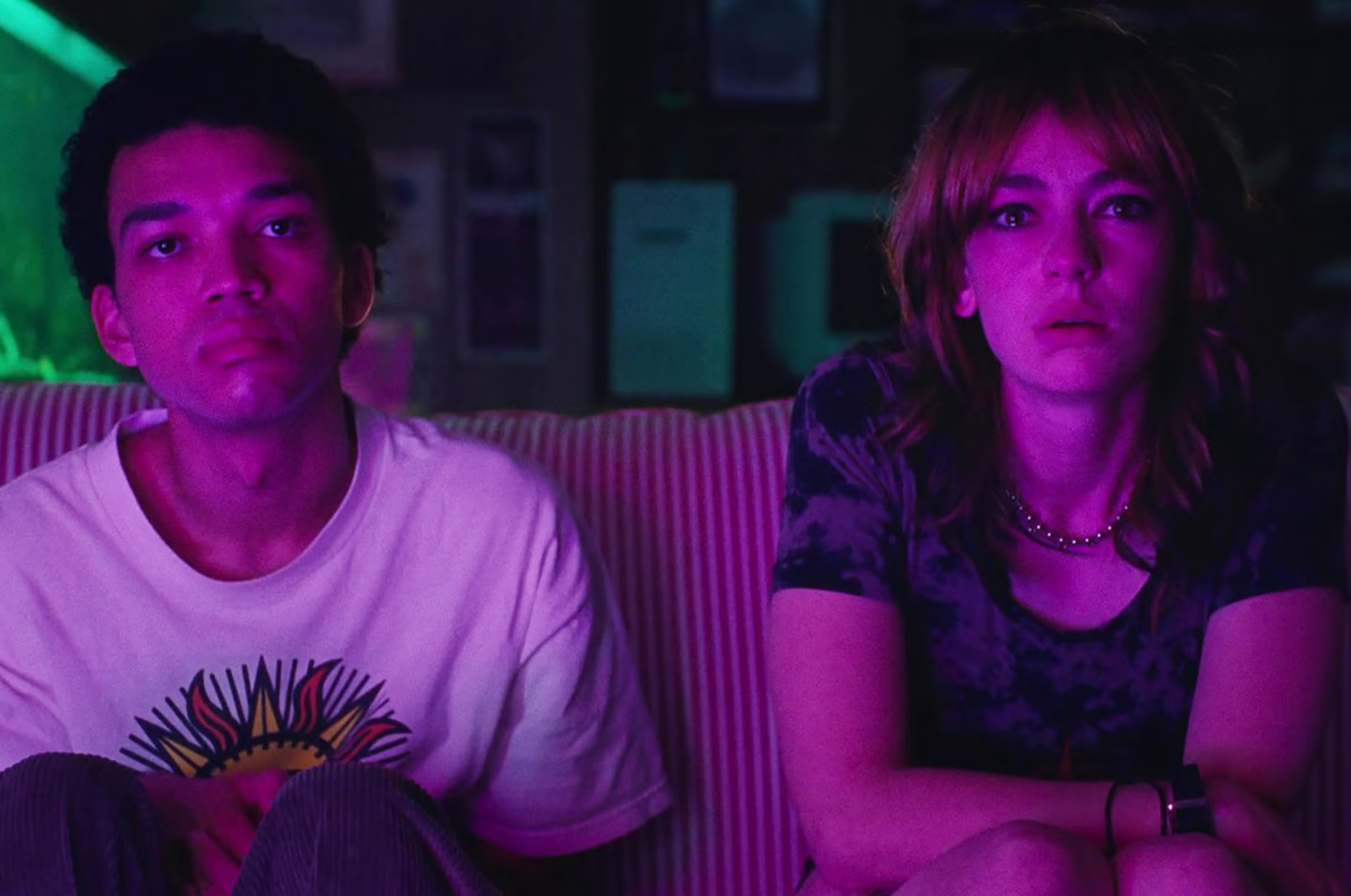 two teenagers watch a screen, lit in pink light, overwhelmed with emotion.