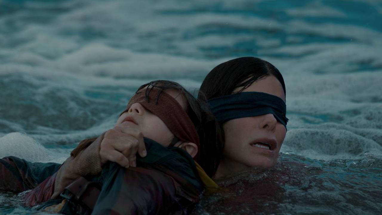 A blindfolded woman clutches a blindfolded child while trying to keep her head above foamy water.