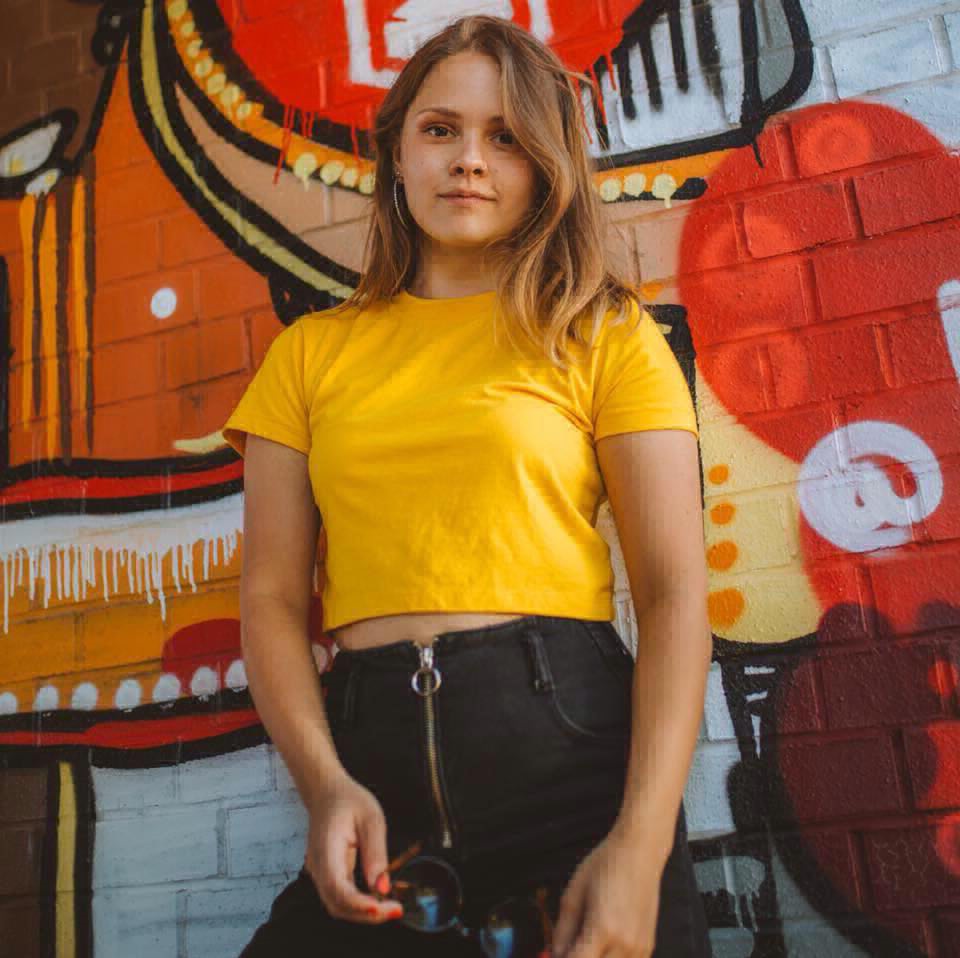 A woman standing in front of a graffitied wall.