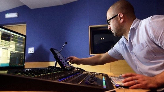 A man in glasses in a sound recording studio, turning a dial.