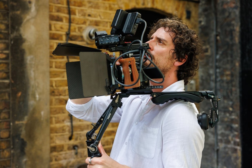 A man with curly hair holding a professional video camera